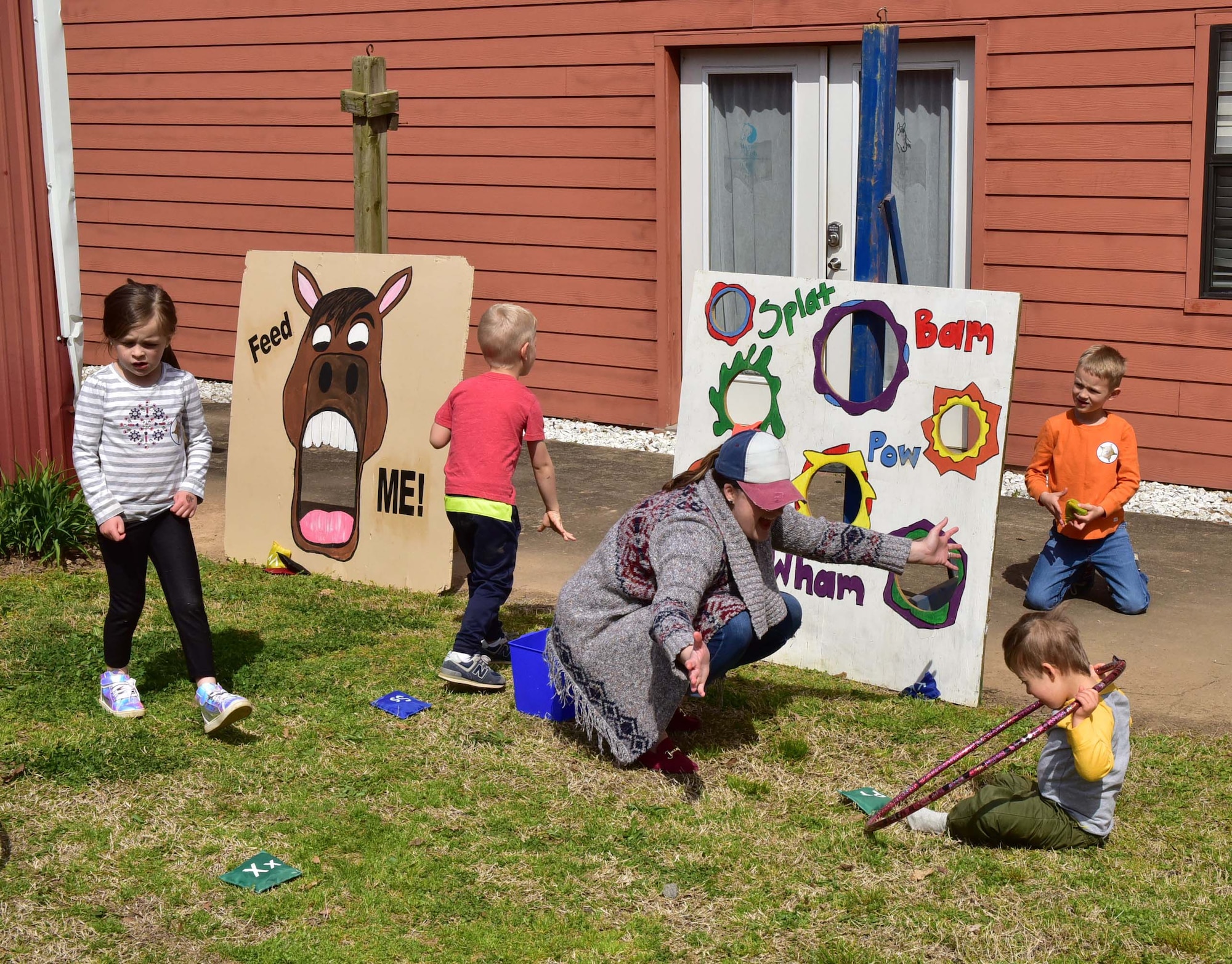 One female adult and four children play on the grass in front of a building.