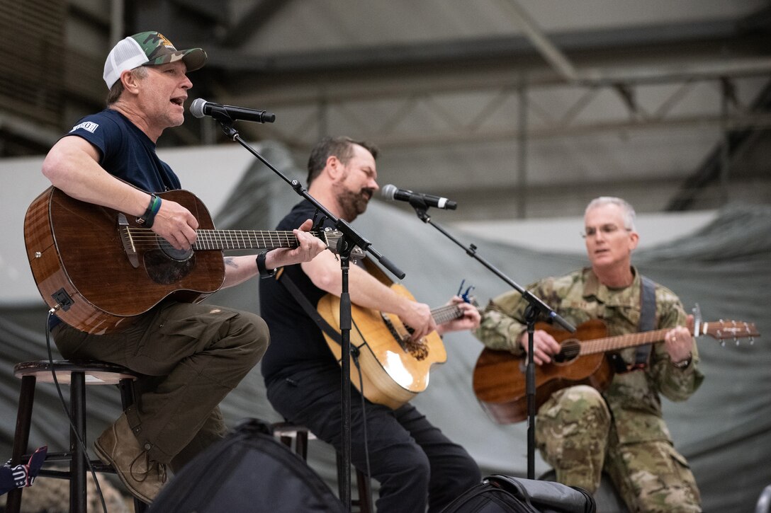 Three men play guitar on a stage.