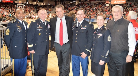 CSM Torenzo Davis, MG Troy Kok, Mr. Mike Bohn, MAJ Ryan Blake, SGM Kimberly Hart, Mr. Stephen Lee- photo taken end court during pregame for the University of Cincinnati basketball game. 6 people gather for a group photo on the bearcats basketball floor. Three men are in uniform, one female in dress blue army uniform. The man in the middle is wearing a black suit and red tie.