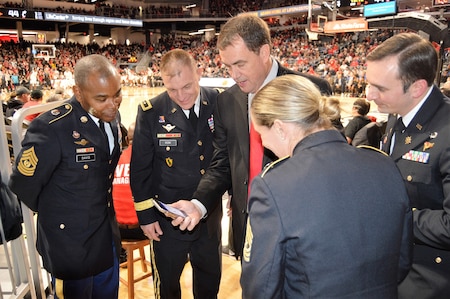 Left to right; CSM Torenzo Davis, MG Troy Kok, Mr. Mike Bohn, SGM Kimberly Hart, MAJ Ryan Blake- Mr. Mike Bohn sharing photos from his cellular phone from his recent visit to the Pentagon during the pregame of the University of Cincinnati basketball game. Men and woman in Army dress blue uniform staring at a cell phone during a college basketball game on the courtside.