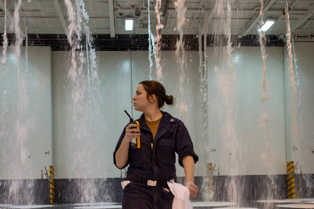 A service member walks in the hangar bay of a ship.