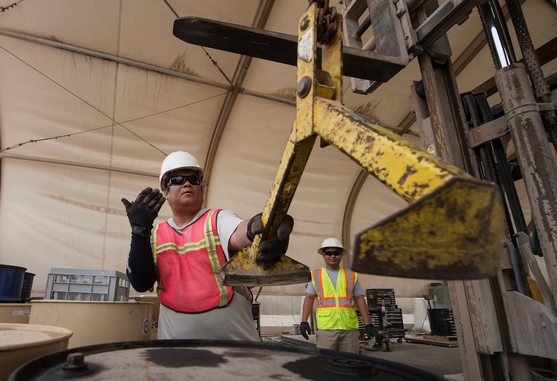 Marino Menor, left, 379th Expeditionary Civil Engineer Squadron (ECES) lead environmental technician, and Jerome Pineda, 379th ECES environmental technician, guide the movement of equipment needed to ventilate an oil drum March 26, 2019, at Al Udeid Air Base, Qatar. Recyclable items such as glass and plastic bottles that are thrown in trash dumpsters at Al Udeid are sorted and recycled at locations off the installation. (U.S. Air Force photo by Tech. Sgt. Christopher Hubenthal)