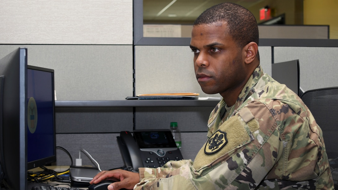 Army Master Sgt. Kahlil Warner works at his computer, seated at his desk