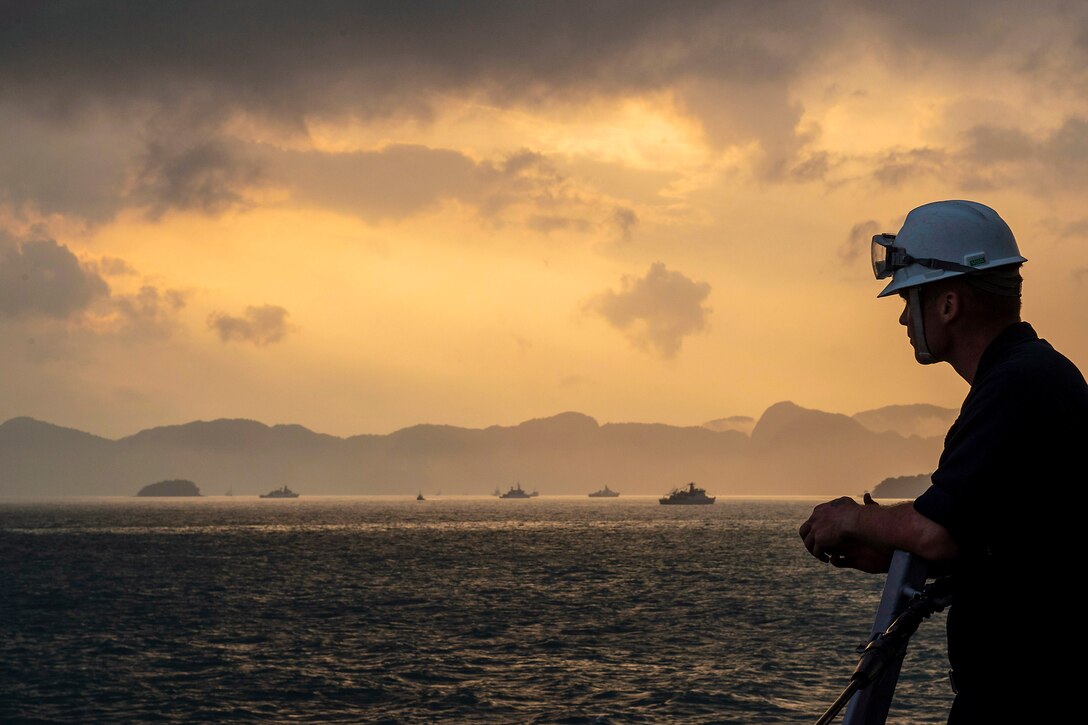 A sailor looks out towards ships anchored in the waters.