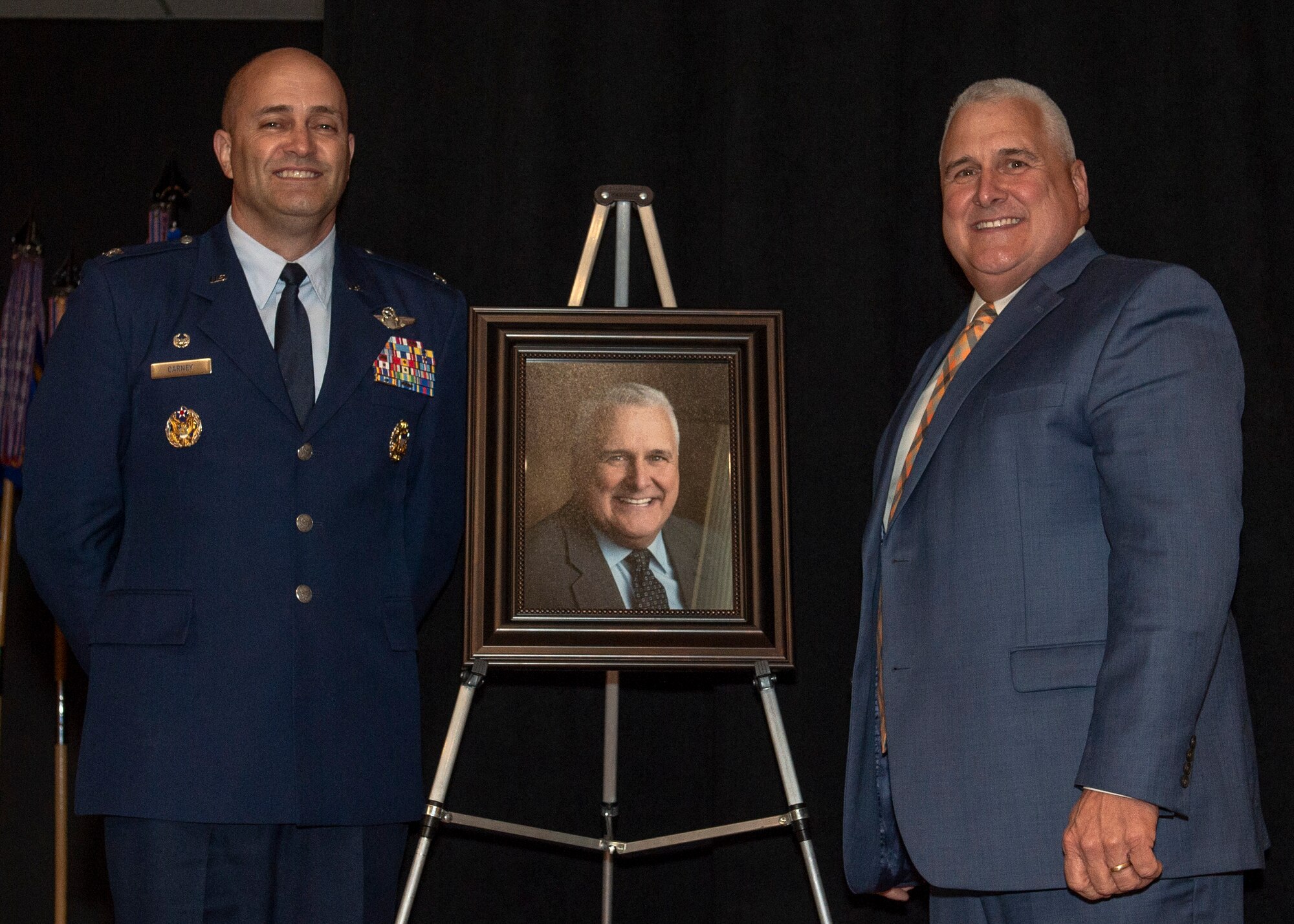 U.S. Air Force Col. Eric Carney, 97th Air Mobility Wing commander, and the Honorable Mike Schulz, former United States Senator for the state of Oklahoma, stand by his portrait during the Friends of Altus Induction ceremony, March 29, 2019, at Altus Air Force Base, Okla. Schulz aided the wing in solving a wind farm crisis that could have affected the training mission of the 97th AMW. (Senior Airman Jackson N. Haddon)