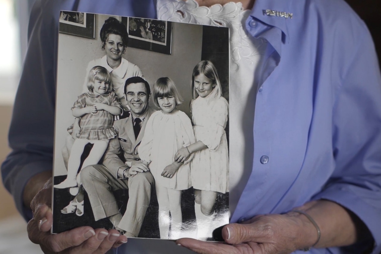 A woman holds a black-and-white photo of a family from the 1970s.