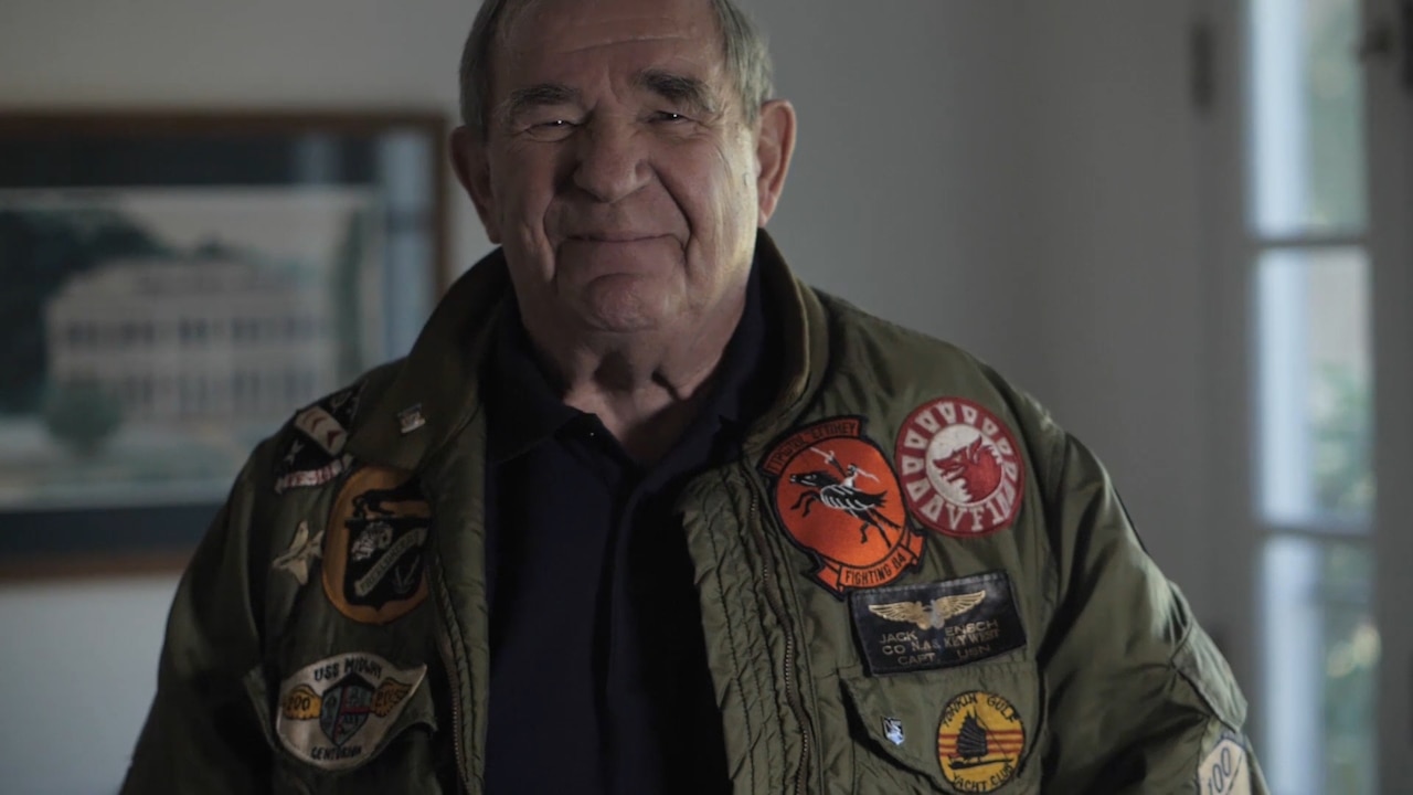 A man poses for a photo wearing a flight jacket covered in patches.