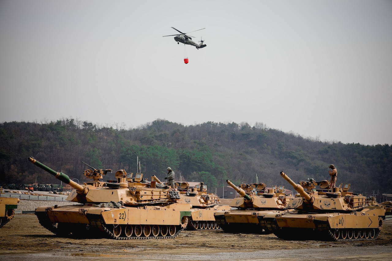 A helicopter flies over tanks.