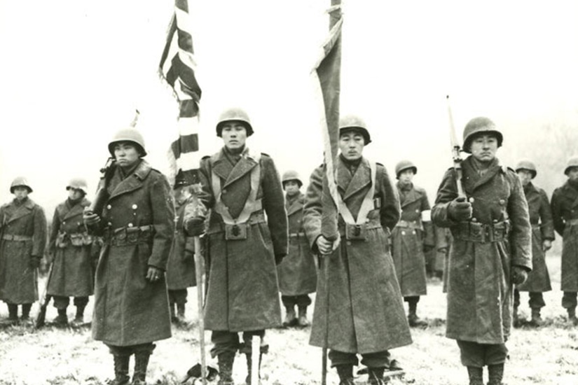 A Nisei color guard stands attention in a field.