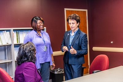 Two ladies stand speaking to a woman that is seated