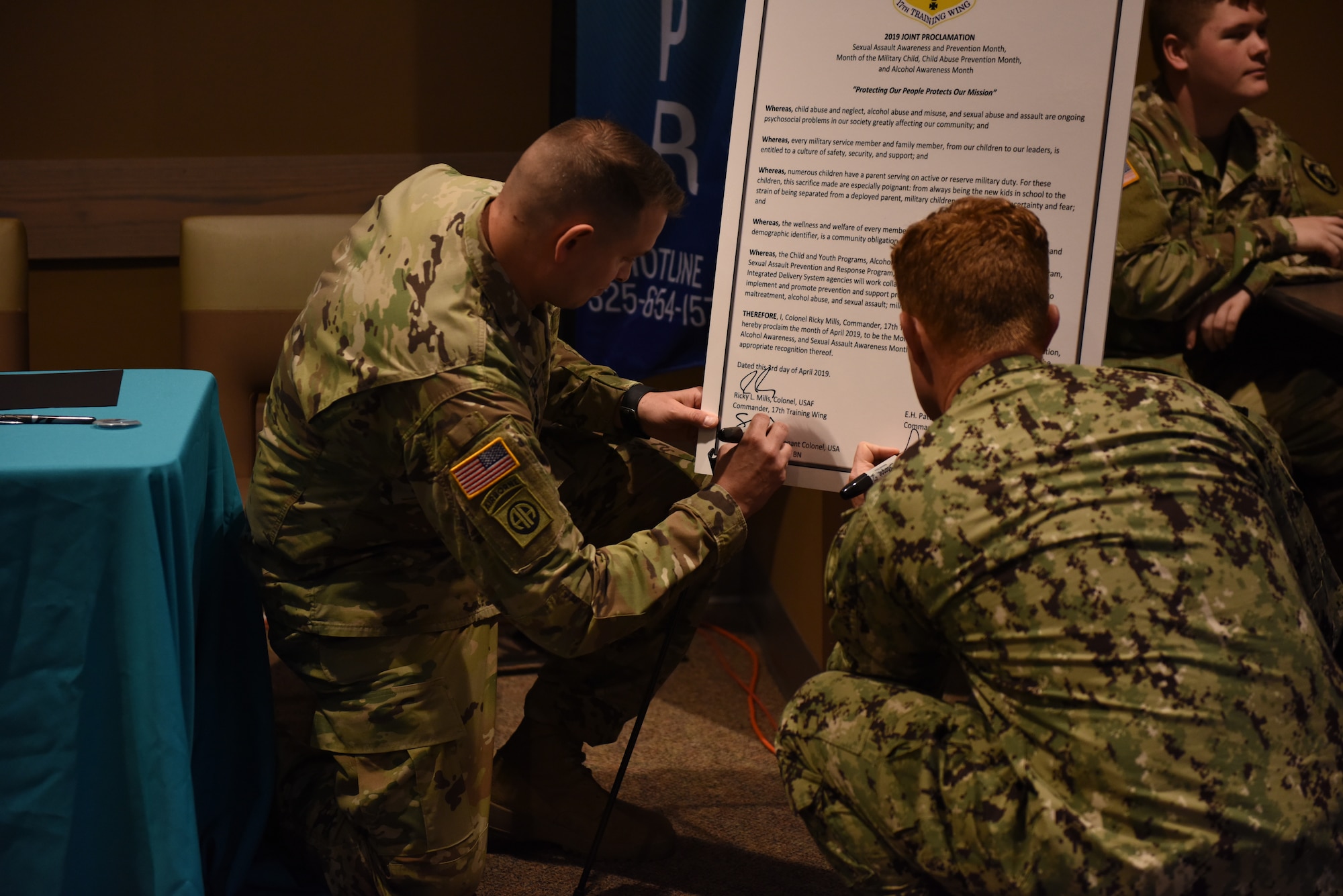 U.S. Army Maj. Shawn Lynch, 344th Military Intelligence Battalion executive officer, and Lt. Cmdr. J. Austin Maxwell, Navy Center for Information and Warfare Training Detachment, sign the proclamation outlining the observances that will be held in April at the Western Winds Dining Facility on Goodfellow Air Force Base, Texas, April 3, 2019. There will be events around base throughout the month of April in support of the observances. (U.S. Air Force photo by Senior Airman Seraiah Hines/Released)