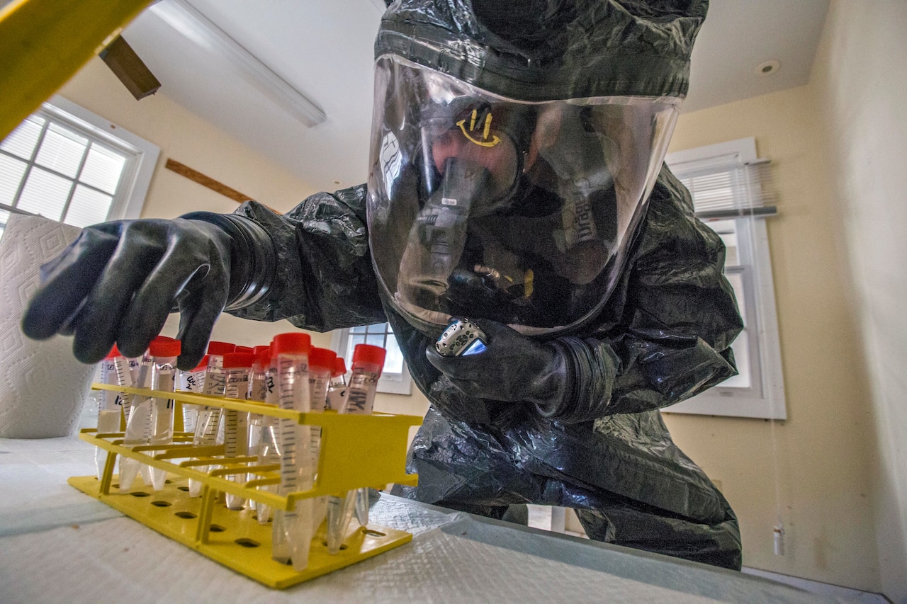 A man in a protective suit inspects vials.