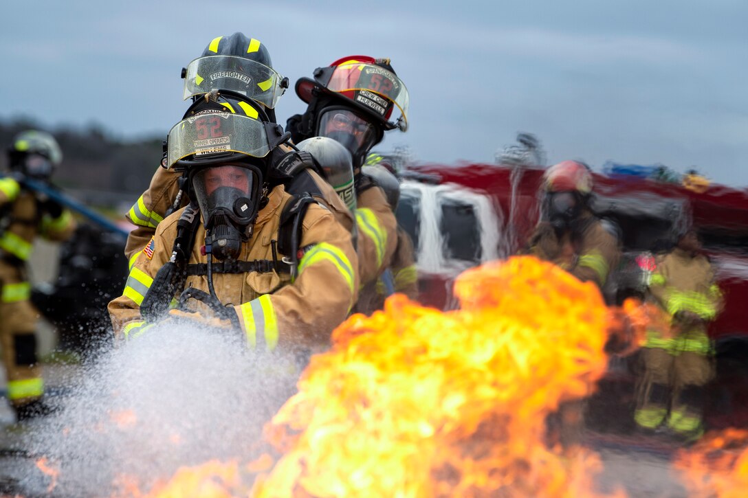 Three airmen hold a fire hose as it sprays water onto a fire.