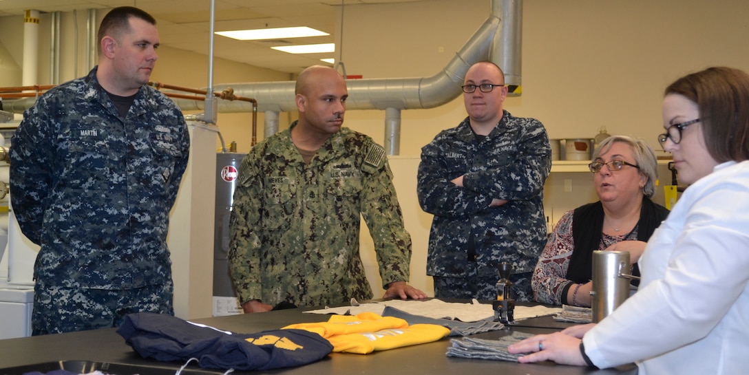 DLA Troop Support Product Test Center Analytical textile technologist Anna Wilson, far left, and lab supervisor Jamie Hieber, second from right, explain how the PTC-A testing processes aided in better adherence of reflective lettering on Navy physical training uniforms to a group of sailors assigned to Naval Support Activity Philadelphia April 3, 2019 in Philadelphia.
