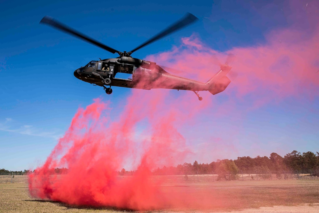 A helicopter preparing to land with pink smoke coming off the ground.