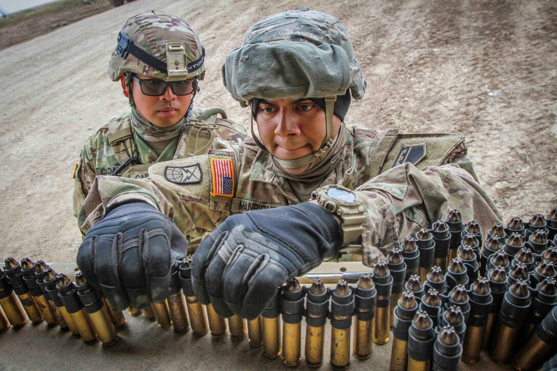 One soldier arranges ammunition into rows while another soldier watches from behind.