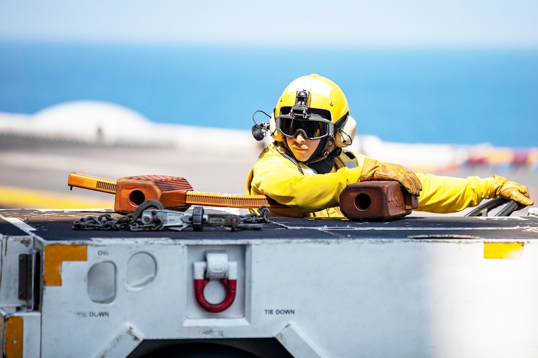 A sailor drives a tractor on a flight deck.