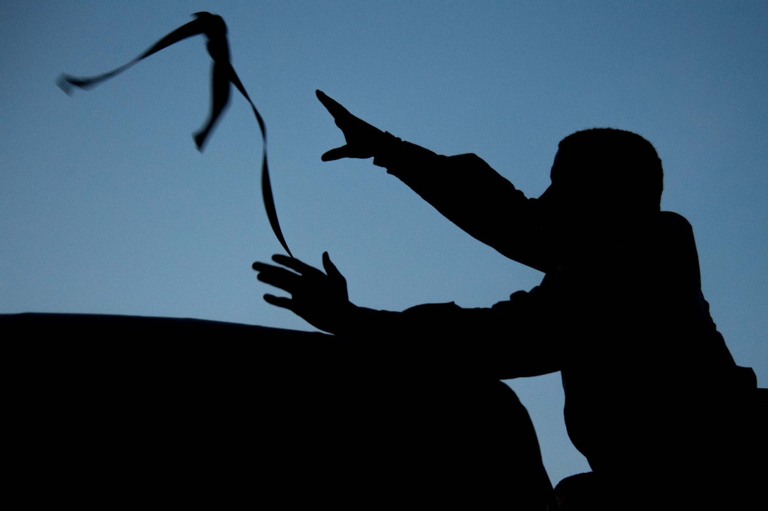 A silhouette of a man throwing  a strap over the engine of an airplane.