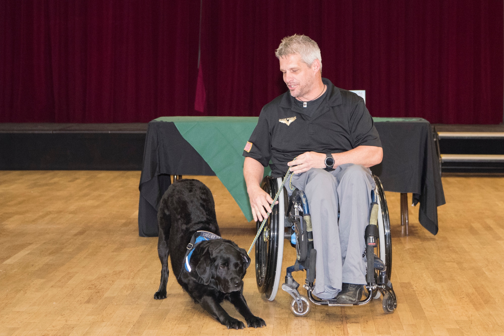 Retired Staff Sgt. Jason Morgan gives his service dog the command to lie down while sharing his story with audience members for a resiliency event on Ramstein Air Base, Germany, April 3, 2019. Morgan became paralyzed from the waist down after the vehicle he rode in careened off a cliff. Despite numerous setbacks, including a leg amputation, he competed and medaled in the U.S. Warrior Games and finished the Marine Corp Marathon in Washington, D.C. (U.S. Air Force photo by Airman 1st Class Kristof J. Rixmann)