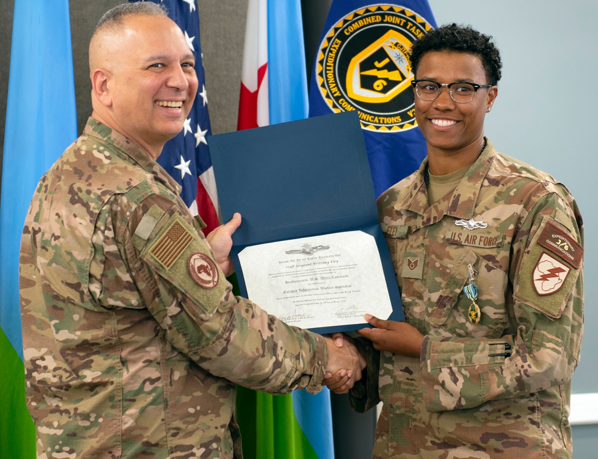 Air Force Col. Kjäll Gopaul (left), communications director for Combined Joint Task Force-Horn of Africa (CJTF-HOA), presents a U.S. Navy enlisted information warfare specialist (EIWS) certificate to Air Force Staff Sgt. Brittany Eley, Joint Network Control Center team lead assigned to CJTF-HOA, at Camp Lemonnier, Djibouti, April 1. Eley has been recognized as the first sister-service EIWS in CJTF-HOA, which signifies that an eligible Sailor has achieved a level of excellence and proficiency in their rating.
