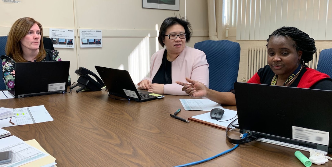 Photo of three females sitting at a table with their laptops having a meeting