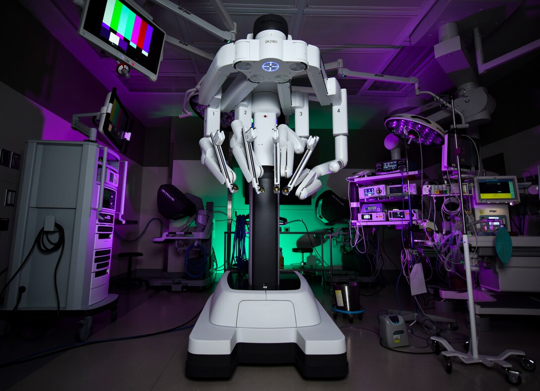The da Vinci Surgery System sits in an operating room illuminated with colorful lights.