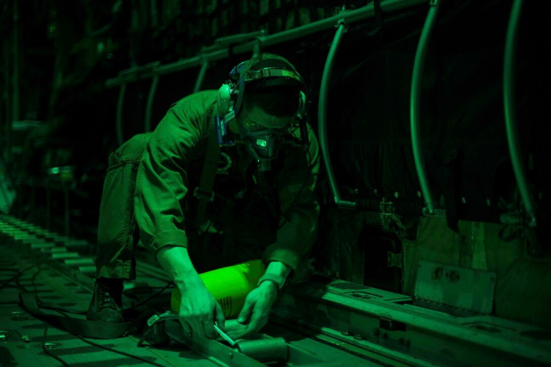 A Marine bent over working on the floor of a plane.