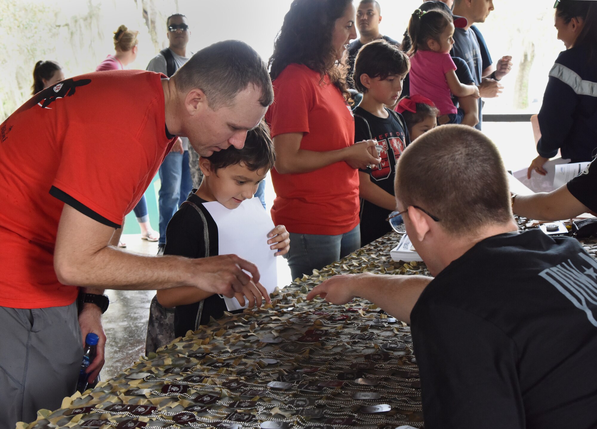 U.S. Air Force Capt. Michael Blank, 81st Medical Operations Squadron nurse, helps his son, Carson, choose an event dog tag during Operation Hero at Keesler Air Force Base, Mississippi, April 6, 2019. The event, hosted by the Airman and Family Readiness Center in recognition of the Month of the Military Child, gave military children a glimpse into the lives of deployed military members. Children received Operation Hero dog tags and t-shirts as they made their way through the mock deployment line as well as the opportunity to experience medical triage demonstrations, gas mask training and have their faces painted. (U.S. Air Force photo by Kemberly Groue)