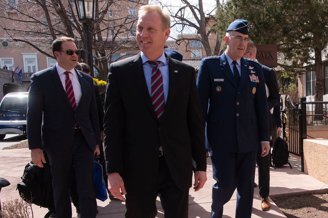 Defense leaders walk together along a sidewalk.