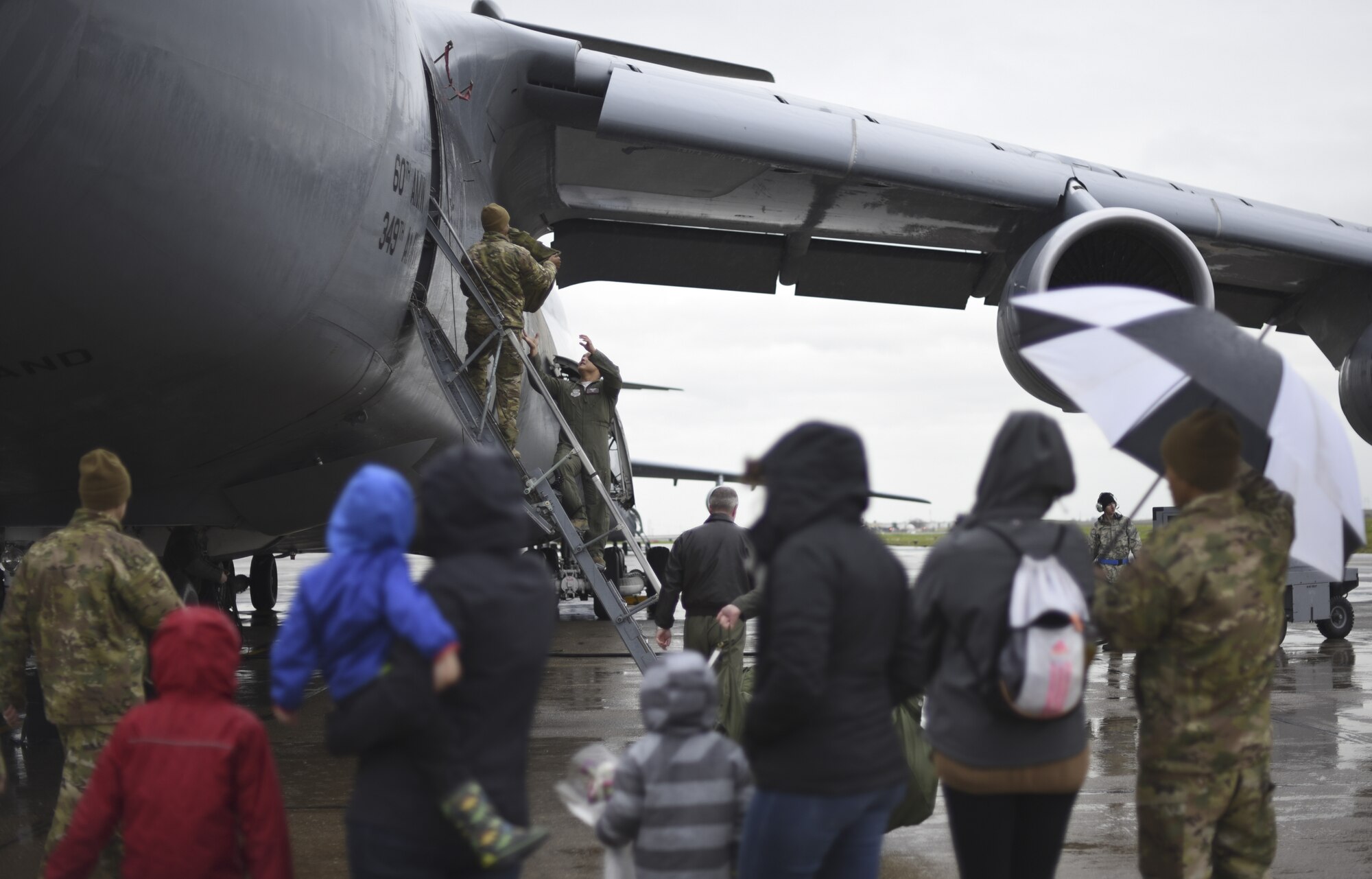 Family members anxiously wait in the rain to greet their Airmen  Feb. 25, 2019,  as they return to Travis Air Force Base, California, from a two-month deployment. The Airmen were part of an air bridge that transported U.S. Army cargo and personnel from Rota, Spain, to Afghanistan as part of a joint operation multimodal mission. (U.S. Air Force photos by Staff Sgt. Amber Carter)
