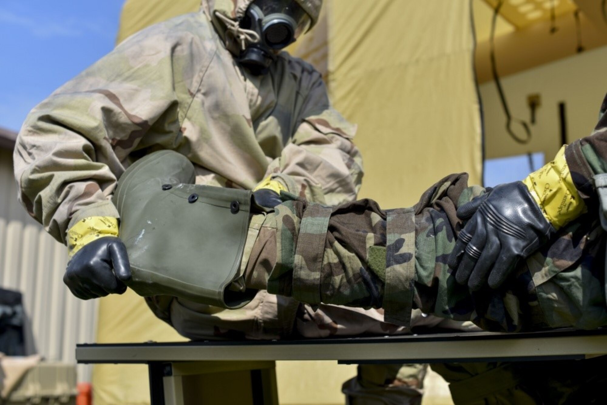 166th Airlift Wing explosive ordnance team leader Staff Sgt. Seth Kohn, left, helps remove the overboot for Staff Sgt. Dominic Buckmuse, right, at the New Castle Air National Guard Base April 7. EOD Airmen work in pairs to decontaminate clothing, as it reduces the chances of contaminating surfaces not exposed to a chemical or biological agent. These practice munitions are not harmful, but Airmen still treat the situation as a realistic training environment. (U.S. Air Force Photo by Capt. Logan Clark)