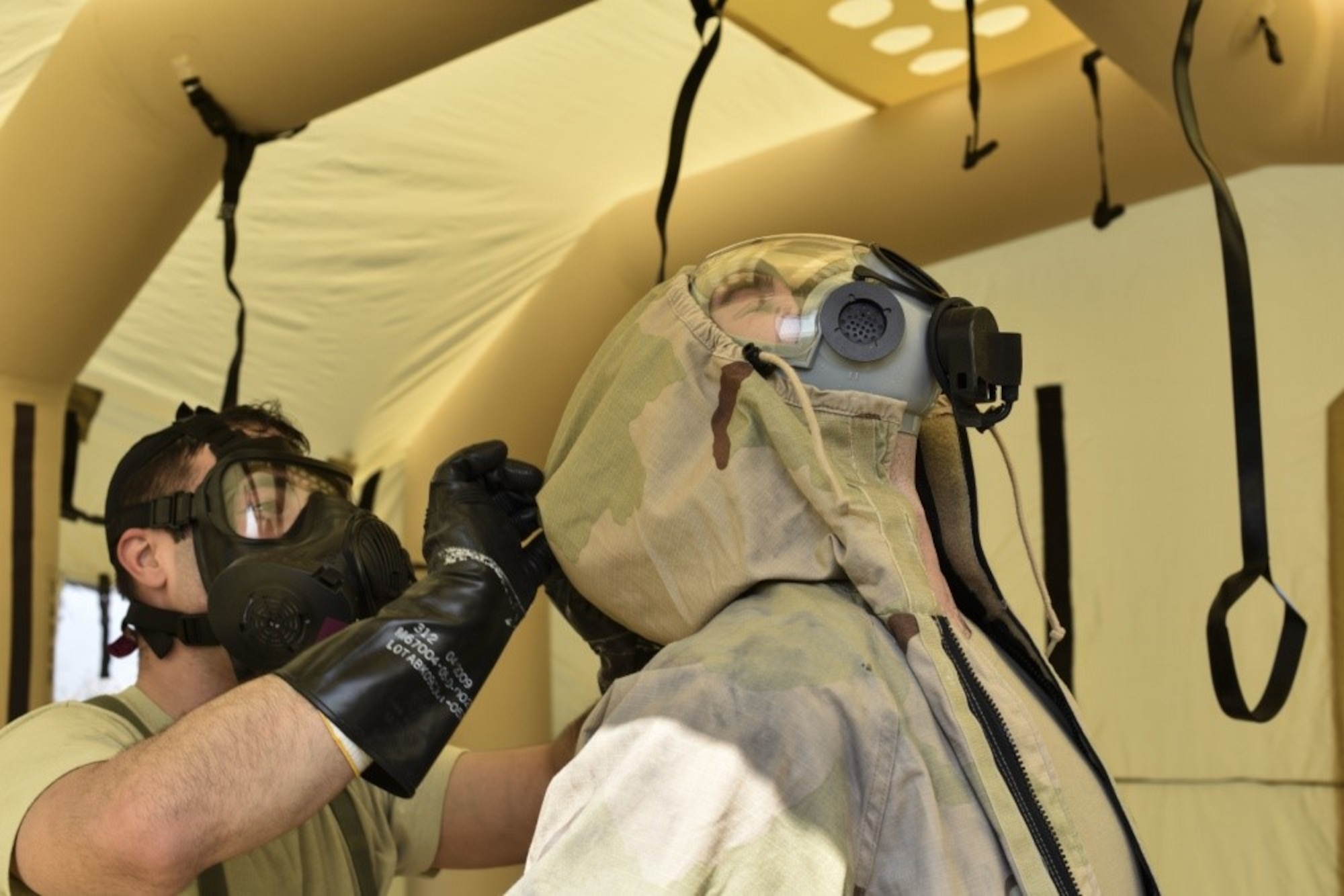 166th Airlift Wing explosive ordnance technician Staff Sgt. Dominic Buckmuse, left, helps remove the protective overcoat of team leader Staff Sgt. Seth Kohn, right, while practicing decontamination procedures at the New Castle Air National Guard Base April 7. EOD Airmen work in pairs to decontaminate clothing, as it reduces the chances of contaminating surfaces not exposed to a chemical or biological agent. These practice munitions are not harmful, but Airmen still treat the situation as a realistic training environment. (U.S. Air Force Photo by Capt. Logan Clark)