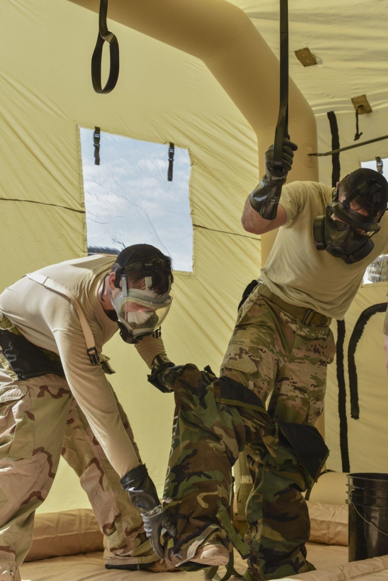 166th Airlift Wing explosive ordnance team leader Staff Sgt. Seth Kohn, left, helps remove the protective pants of technician Staff Sgt. Dominic Buckmuse, right, while practicing decontamination procedures at the New Castle Air National Guard Base April 7. EOD Airmen work in pairs to decontaminate clothing, as it reduces the chances of contaminating surfaces not exposed to a chemical or biological agent. These practice munitions are not harmful, but Airmen still treat the situation as a realistic training environment. (U.S. Air Force Photo by Capt. Logan Clark)