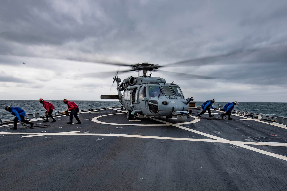 Sailors remove chains from a helicopter.