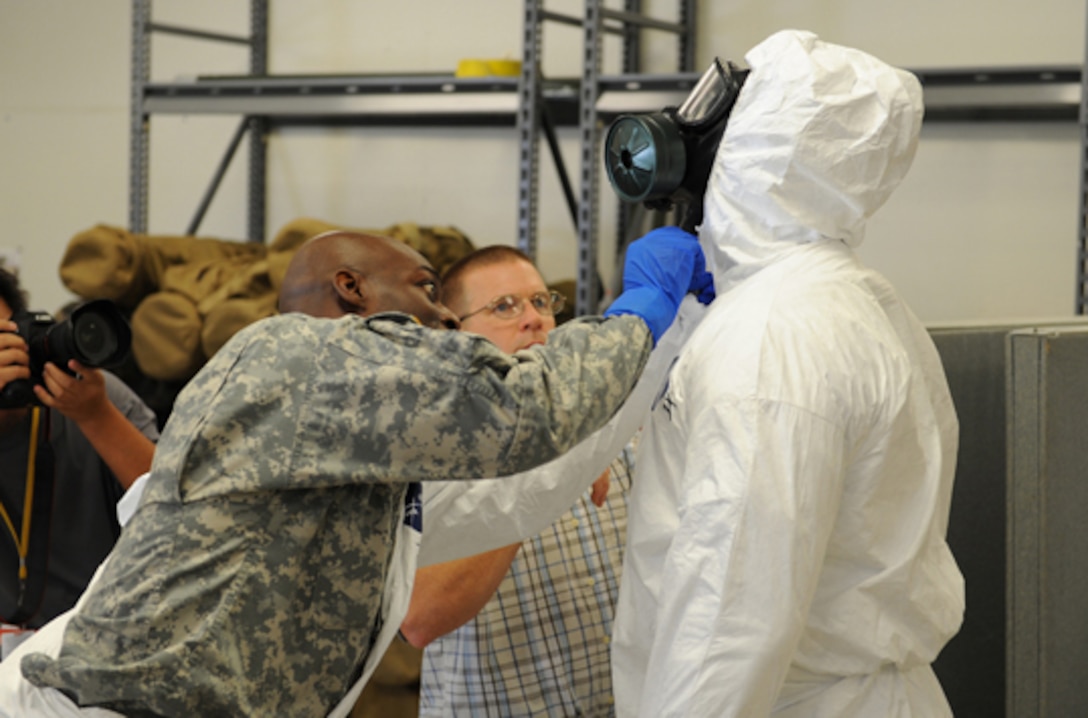 Army Maj. John Dills, the 36th Engineer Brigade chief of current operations, left, helps zip and close Sgt. 1st Class Venrick James’, a 36th Engineer Brigade soldier, right, Tyvek protective suit around his M40 protective mask during training inside the Medical Skills Training Center at Fort Hood, Texas.