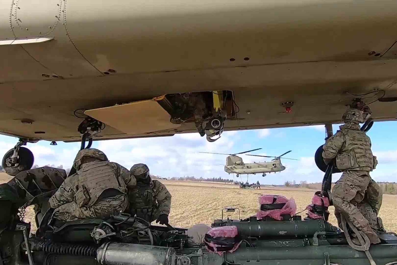 Soldiers connect an M777 howitzer cannon to a CH-47 Chinook helicopter