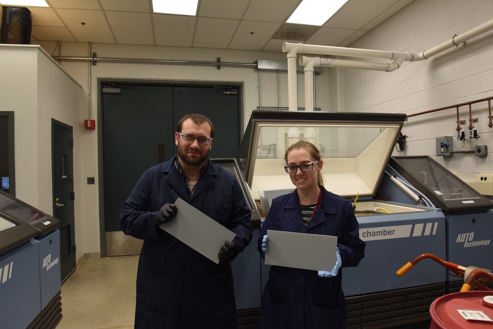 Chemist Dr. Kylee Fazende (right) and Engineer Dr. Charles White hold test-ready paint panels in Naval Surface Warfare Center Carderock Division’s accelerated exposure and weathering lab in West Bethesda, Md., on April 4, 2019. (U.S. Navy photo by Edvin Hernandez/Released)