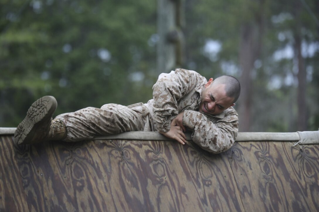 A recruit winces and uses his boot heel to pull himself over an  obstacle.