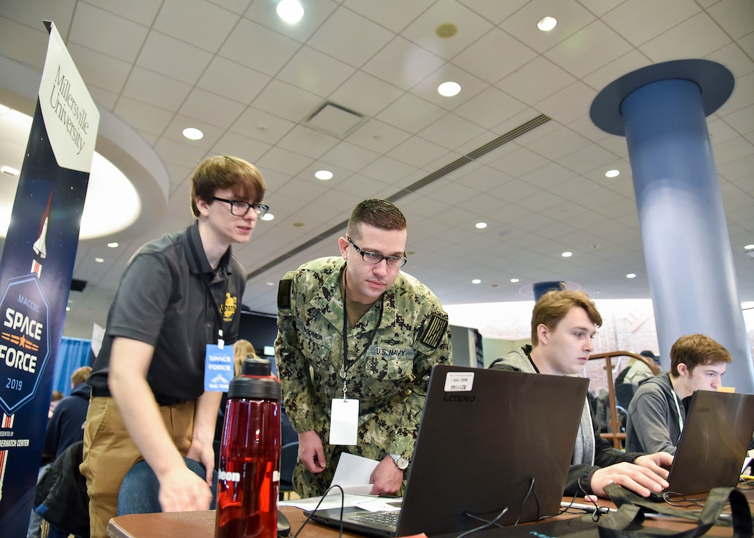 Greg Bodmer, Cryptologic Technician (Networks) assigned to Cyber Defense Activity - 64, Fort Meade, Md., examines a participants monitor during the 14th Annual Mid-Atlantic Collegiate Cyber Defense Competition Regional Finals, March 29, 2019 at Johns Hopkins University Applied Physics Laboratory, Laurel, Md. Each year all participants are divided into three teams with specific responsibilities. (U.S. Air National Guard photo by Staff Sgt. Enjoli Saunders)