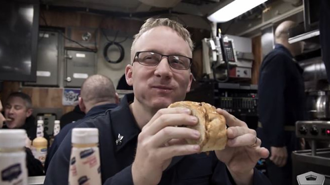 A sailor smiles while eating.
