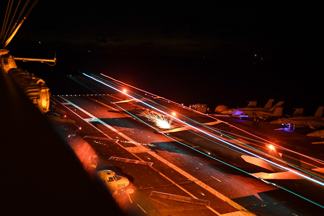 An aircraft lands onto a ship at night.