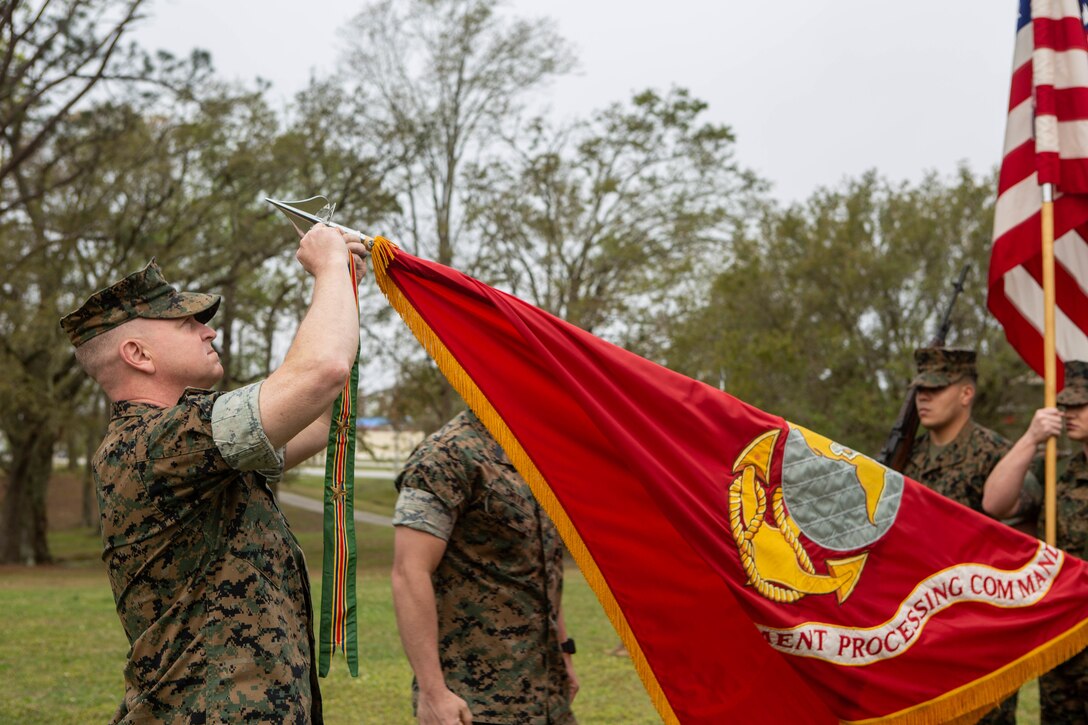 Colonel Michael J. Corrado, commanding officer, Deployment Processing Command / Reserve Support Unit-East, adds a meritorious unit commendation streamer with three bronze stars to the DPC/RSU-East battle colors during the rededication ceremony for DPC/RSU-East, Camp Lejeune, North Carolina, April 8.  The rededication ceremony was held to celebrate and reflect on the accomplishments of the unit for the past 70 years. (U.S. Marine Corps photo by Lance Cpl. Ashley Gomez)