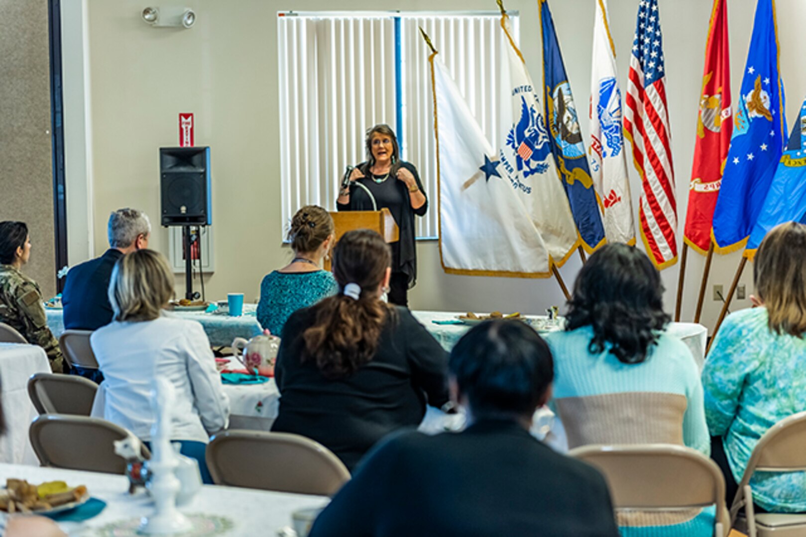 Keynote speaker speaks next to flags to a full room