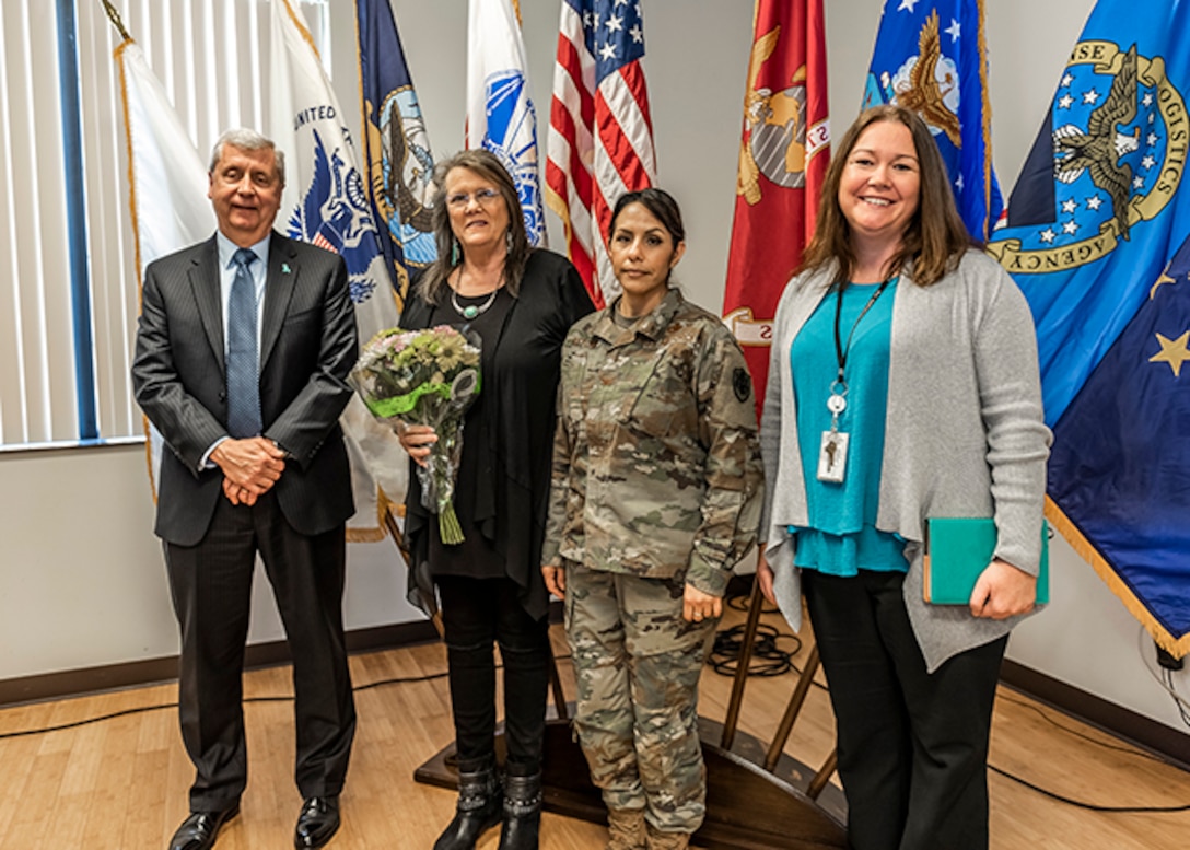 Four people stand for a photo in front of flags