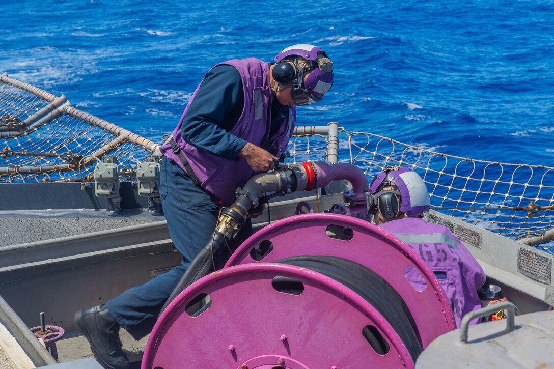 Sailors attach a hose on board a ship.