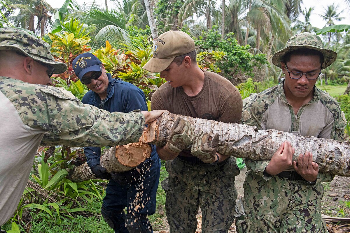 A civilian and sailors clear branches on a path.