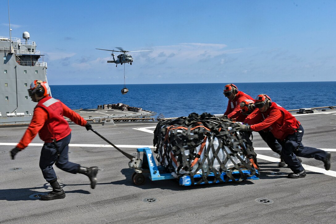 One sailor pulls a package while two others push from the other side.