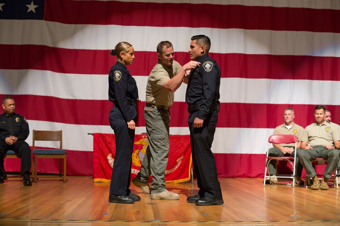 A graduate of Marine Corps Police Academy West is presented with a badge on stage at Marine Corps Air Station Miramar, Calif., April 9. Prior to graduating, recruits go through a 24 week physical training program before earning their badge as an officer in law enforcement. (U.S. Marine Corps photo by Cpl. Nadia J. Stark)