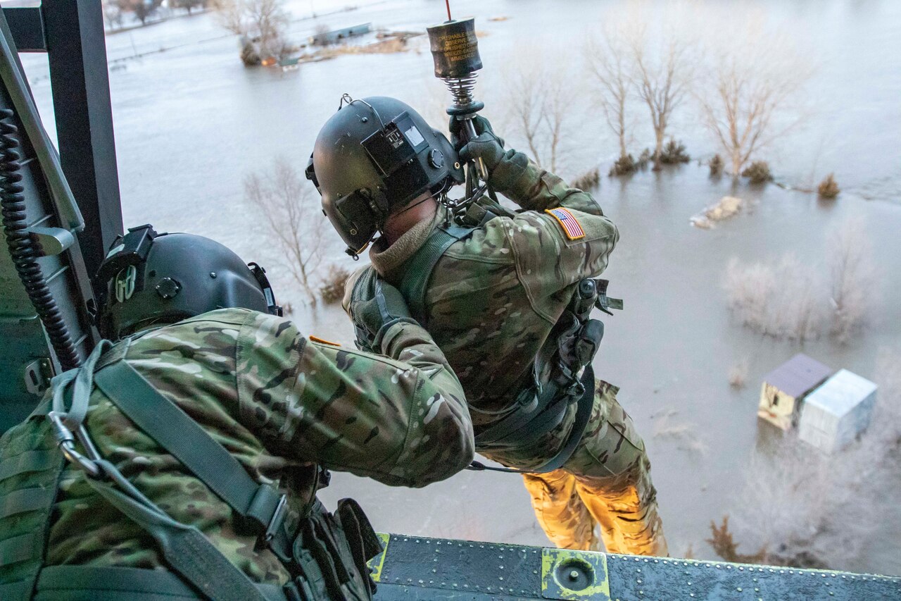 A service member descends from a helicopter.