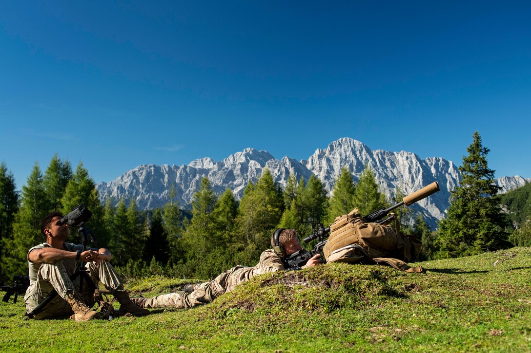 Soldiers aim a gun in the mountains.